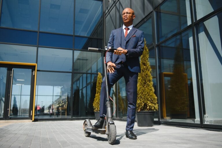 businessman with electric scooter standing in front of modern business building talking on phone.